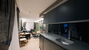 A modern kitchen with dark cabinetry, a stainless steel sink, and a dining area with a round table and chairs. - Marlen Residence Hotel (Izmir)