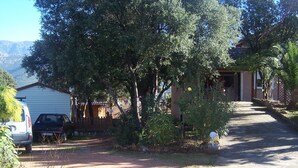 Une allée menant à une maison avec un garage, des voitures garées et une cour clôturée avec des arbres.