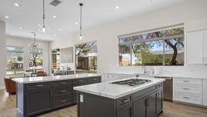 Una cocina moderna con una isla grande, armarios oscuros y ventanas amplias que ofrecen vistas al exterior.