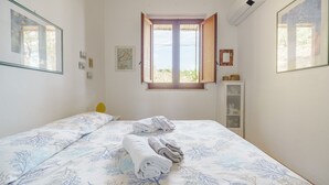 Ein Schlafzimmer mit einem Bett, einem Fenster mit geöffneten Läden und einem kleinen Schrank.