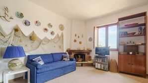 Ein Wohnzimmer mit einem blauen Sofa, einem weißen Beistelltisch, einer blauen Lampe, einem Kamin, einem Fernseher und einem Holzkabinett.