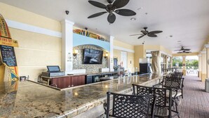 Eine Bar mit einer Theke, Sitzgelegenheiten, Deckenventilatoren und einem Fernsehbildschirm.