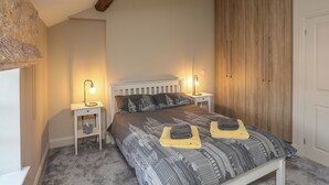A bedroom with a bed, two bedside tables, a wooden wardrobe, and a window with a curtain. - 2 Ivy House (Corwen)