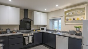A modern kitchen with dark cabinets, a black range hood, a microwave, a sink, and a dishwashing machine. - 2 Ivy House (Corwen)