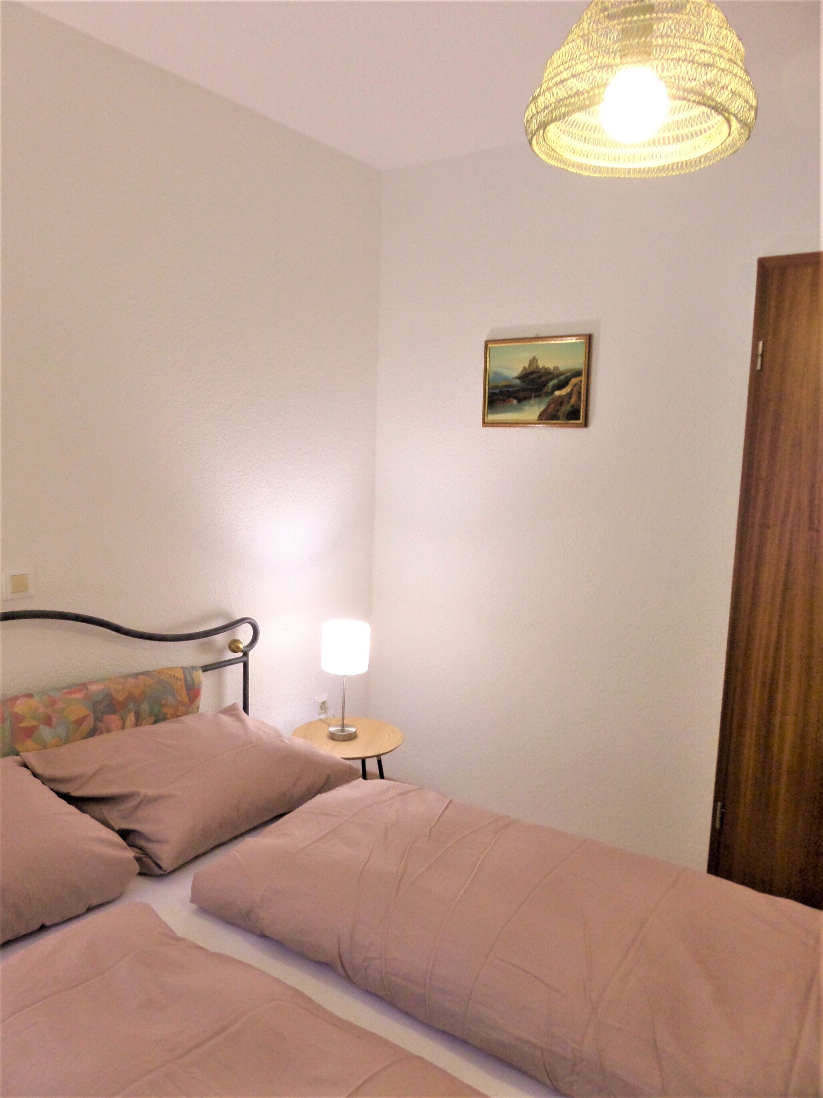 A bedroom with a bed, a bedside lamp, a painting on the wall, and a wooden door.