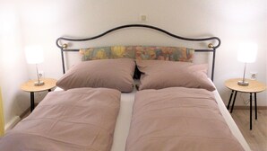 A single bed with a metal frame, two pillows, and a headboard with a floral design. There are two bedside tables with lamps. - Apartment Bergblick in an idyllic location on the edge of the forest, 5 min. to the waterfall (Triberg im Schwarzwald)