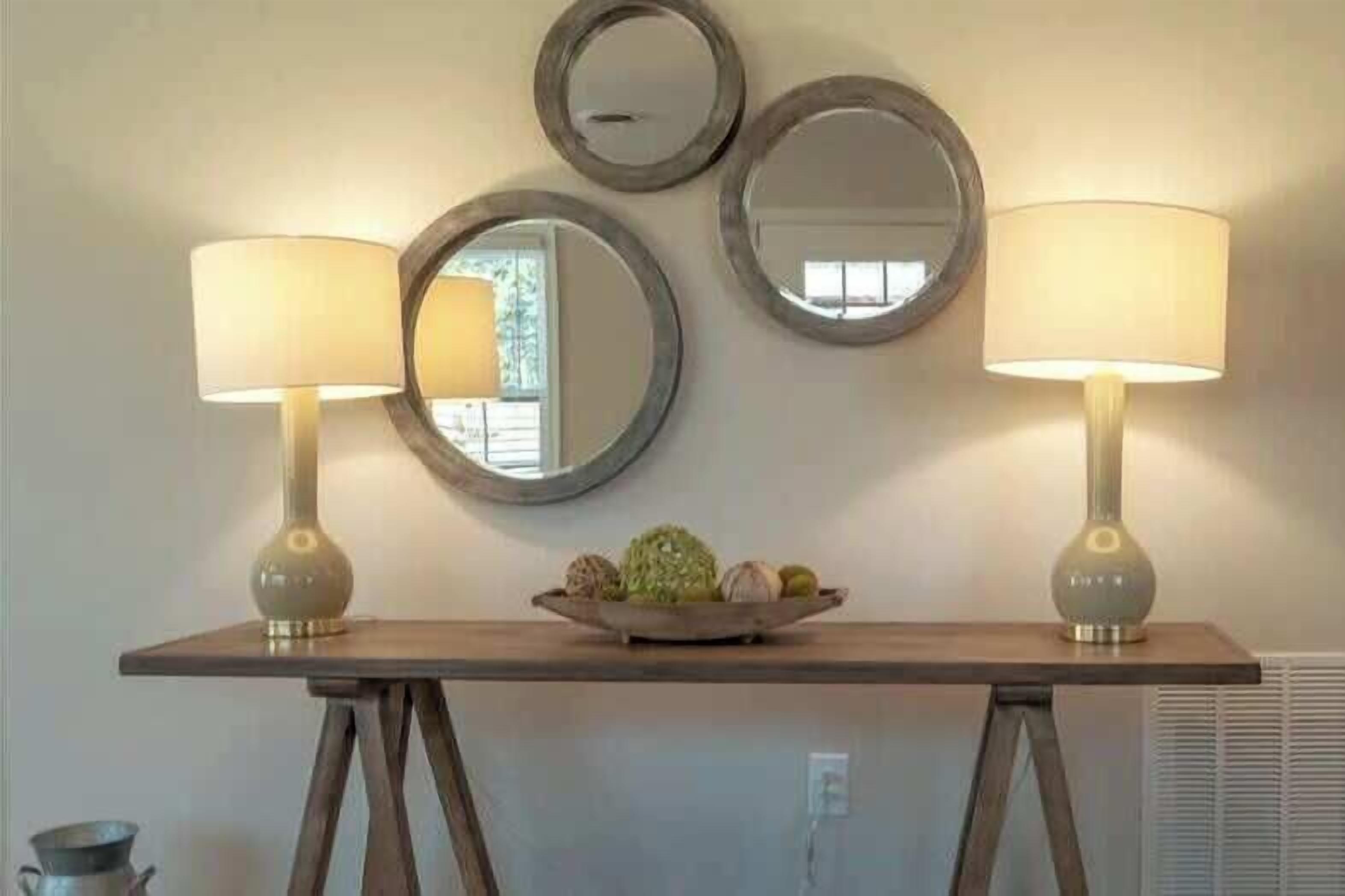 Une pièce avec une table en bois, deux lampes et trois miroirs fixés au mur.