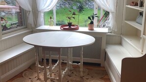 Een gezellige kamer met een witte ronde tafel, een bankje en uitzicht op een tuin door dunne gordijnen.