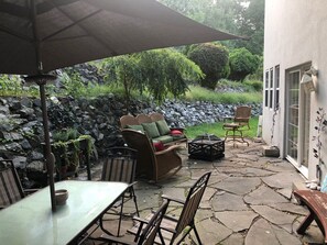 Een terras met stenen vloer, een tafel, stoelen, een bank en een parasol.