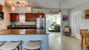 A modern kitchen with granite countertops, wooden cabinets, and stainless steel appliances. There is a bar area with stools and a seating area with a couch and chairs. - 3 Bed 2 Ba, Wifi, Kitchen, Walk to Beach, FirePit (Daytona Beach)