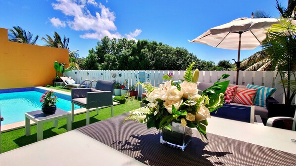 Un jardin avec une piscine, du mobilier d’extérieur et une table agrémentée d’un vase de fleurs.