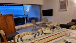 Ein Essbereich mit einem Tisch für vier Personen, einem an der Wand befestigten Fernseher und Meerblick durch eine Glastür.