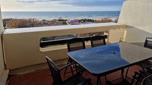 Ein Balkon mit Tisch und Stühlen, mit Blick auf einen Strand und einen Streifen Sonnenschirm.