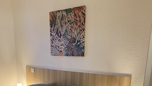 Ein Schlafzimmer mit Bett, Kopfstütze, Nachttisch mit Lampe und floralem Wandbild.