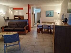 A compact living space with a sofa, a dining table set for four, a kitchenette, and a small kitchen area.
