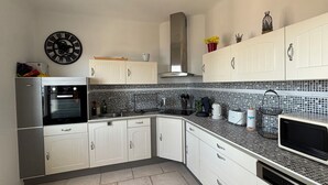 Une cuisine moderne avec des meubles blancs, un dosseret carrelé noir et blanc, un four encastré et un four à micro-ondes.