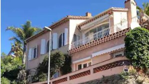 Un immeuble de deux étages avec une façade en pierre, un balcon doté d’une balustrade et une grande porte marron.