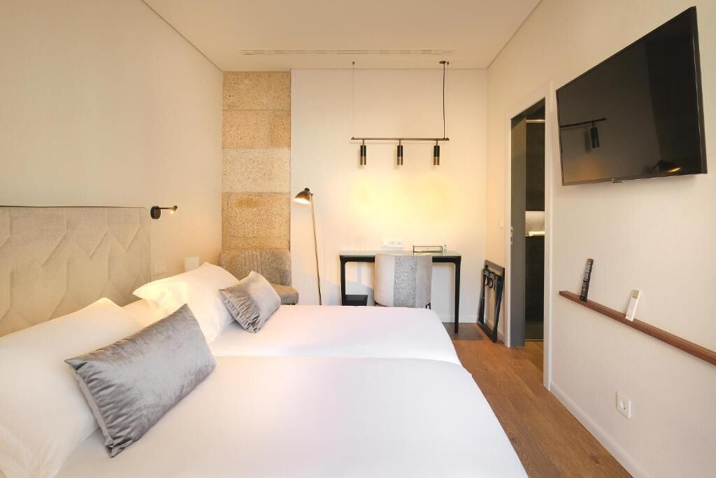 A hotel room with a large bed, a desk, and a TV mounted on the wall.