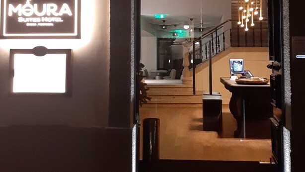 Entrada de un hotel con un cartel que dice "MOURA SUITES HOTEL" y vista del interior que muestra una escalera, un comedor y luces colgantes.
