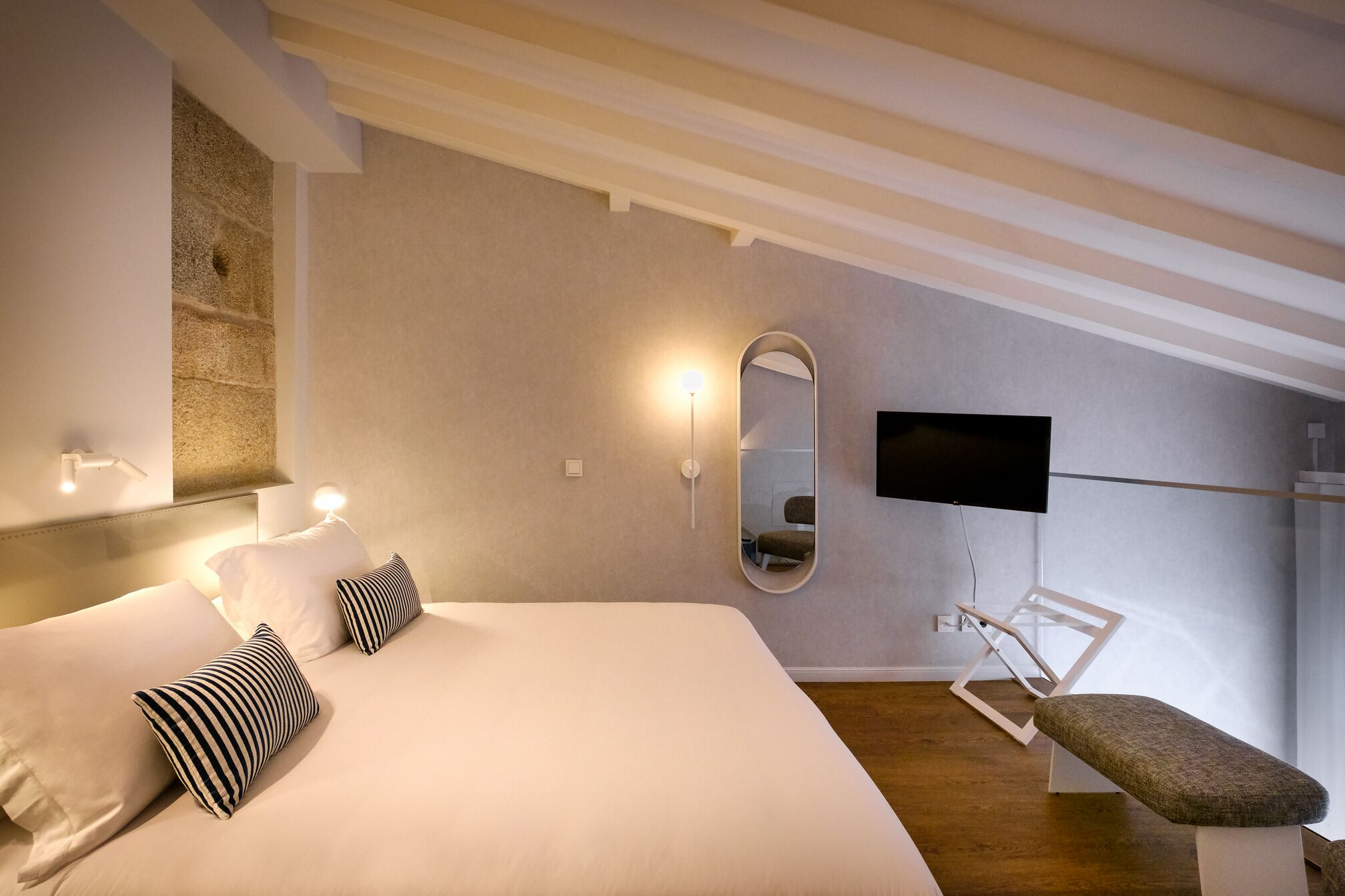 Ein modernes Hotelzimmer mit einem großen Bett, einem Flachbildfernseher, einer Bank und einer Steinwand.
