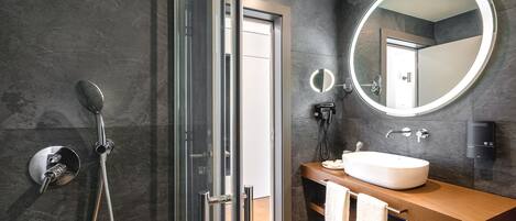 A modern bathroom with a glass-enclosed shower, a round mirror, and a wooden vanity with a sink.