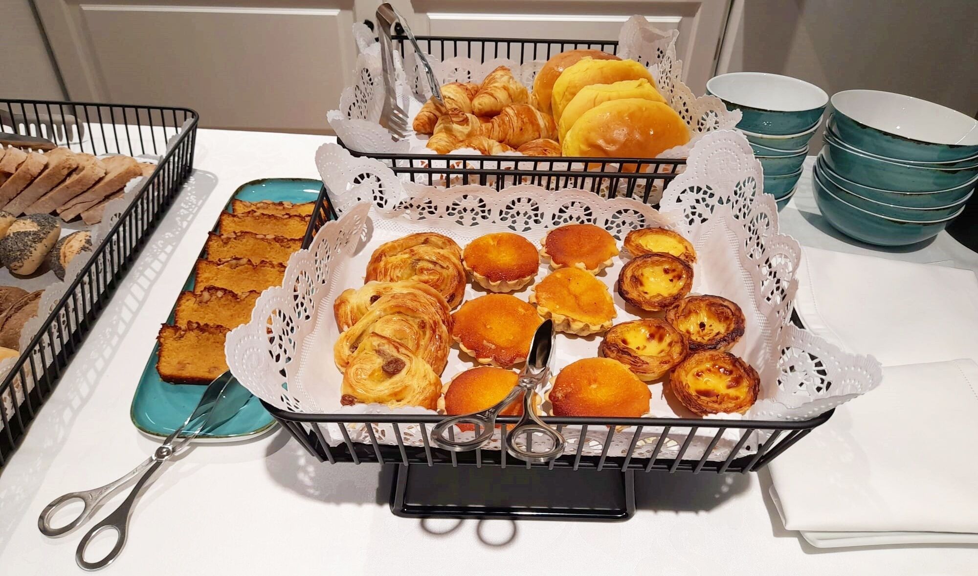 A buffet table with various baked goods including pastries, bread, and rolls.