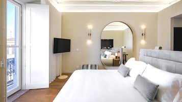 Ein modernes Hotelzimmer mit einem großen Bett, einem an der Wand montierten Fernseher, einem runden Spiegel und Blick auf den Außenbalkon.