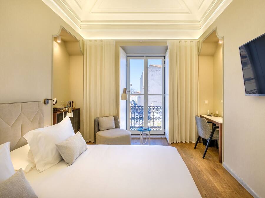 Una habitació d'hotel amb un llit gran, una taula de treball, una cadira i un televisor penjat a la paret.