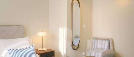 A hotel room with a bed, a chair, a nightstand with a lamp, a mirror, and two wall-mounted lights.