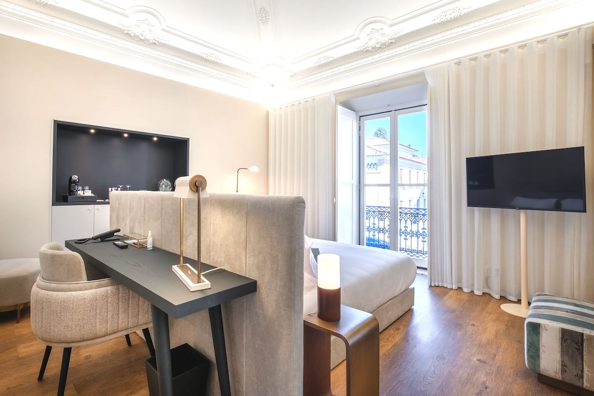 Ein Hotelzimmer mit Bett, Schreibtisch mit Stuhl, Fernseher und einem Balkon mit Vorhängen.
