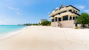 A beachfront property with a multi-story building, a sandy beach, and a clear blue sky. - Oasis 7-stunning private beachfront villa with rooftop pool-by Cayman Villas! (Seven Mile Beach)