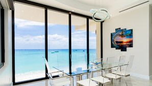 A modern room with a glass table and chairs, a large window with a view of the ocean, and a chandelier. - Oasis 7-stunning private beachfront villa with rooftop pool-by Cayman Villas! (Seven Mile Beach)