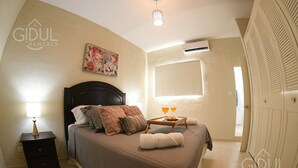 A bedroom with a bed, nightstand, bedside lamp, and a painting on the wall.