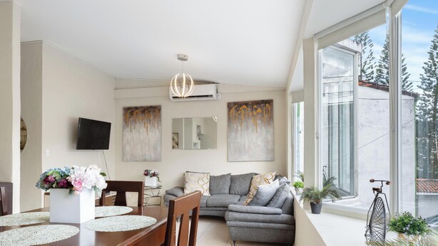 A modern living room with a dining area, large windows, and a balcony with plants.