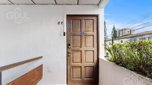 A wooden door with a blue sign, a number '22' on the wall, and a small window with plants.