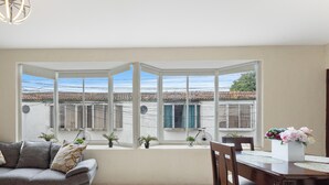 A modern living room with a grey sectional sofa, a dining table with chairs, and a bay window with a view of buildings and power lines.