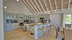 A spacious kitchen with white cabinetry, a central island with bar stools, and a dining area with a table and chairs.