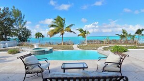 A pool area with lounge chairs and a hot tub, overlooking a beach with palm trees and the ocean.
