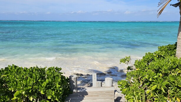 A wooden pathway leading to a beach with clear turquoise water and lush greenery.