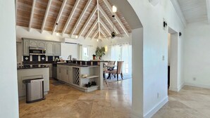 A spacious kitchen with a central island, wooden ceiling beams, and a dining area with a table and chairs.