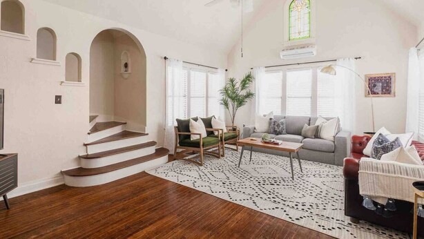 A spacious living room with a staircase, a ceiling fan, and a large window with stained glass. - The Halcyon- a Cozy 2BR Tudor in Crestwood-Sleeps 6! (Oklahoma City)