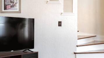 Ein modernes Wohnzimmer mit einem Flachbildfernseher auf einem dunklen Holzschrank, weißen Wänden und einer Treppe mit weißen Stufen.