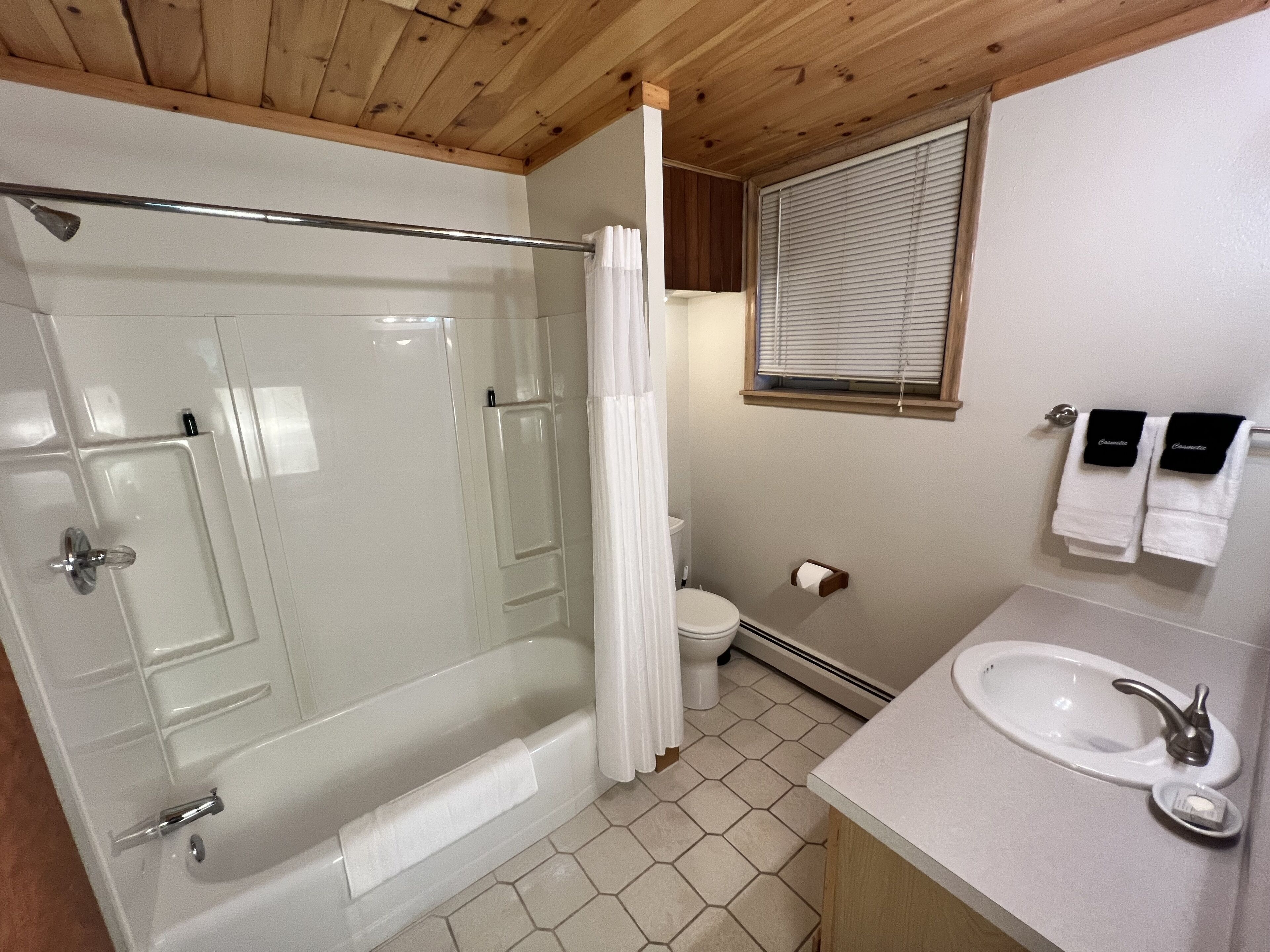 A bathroom with a glass-enclosed shower, a toilet, a sink, and a window with blinds.