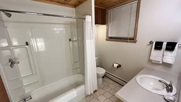 A bathroom with a glass-enclosed shower, a toilet, a sink, and a window with blinds.