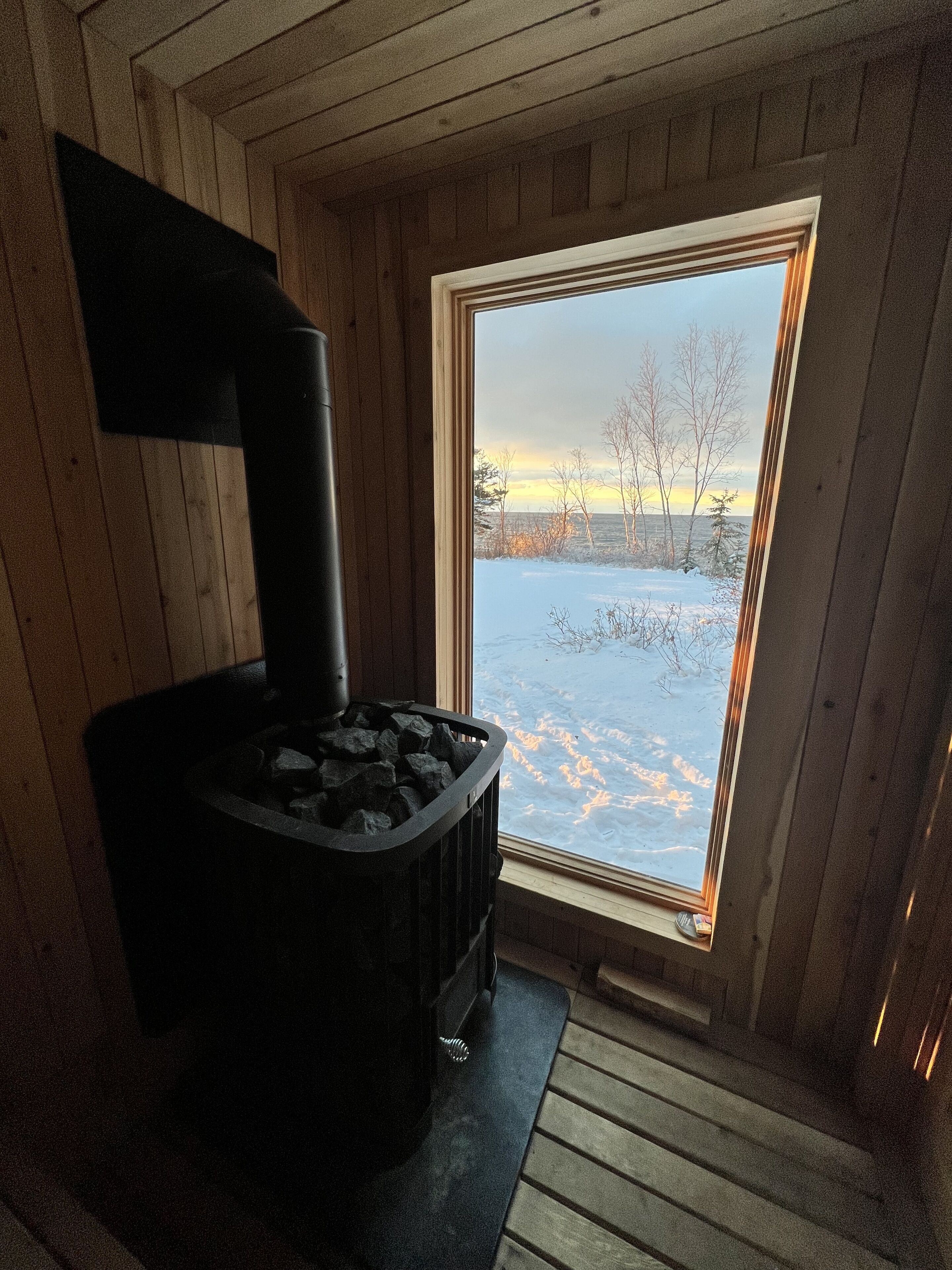 A wood-burning stove in a cabin with a view of a snowy landscape through a window.