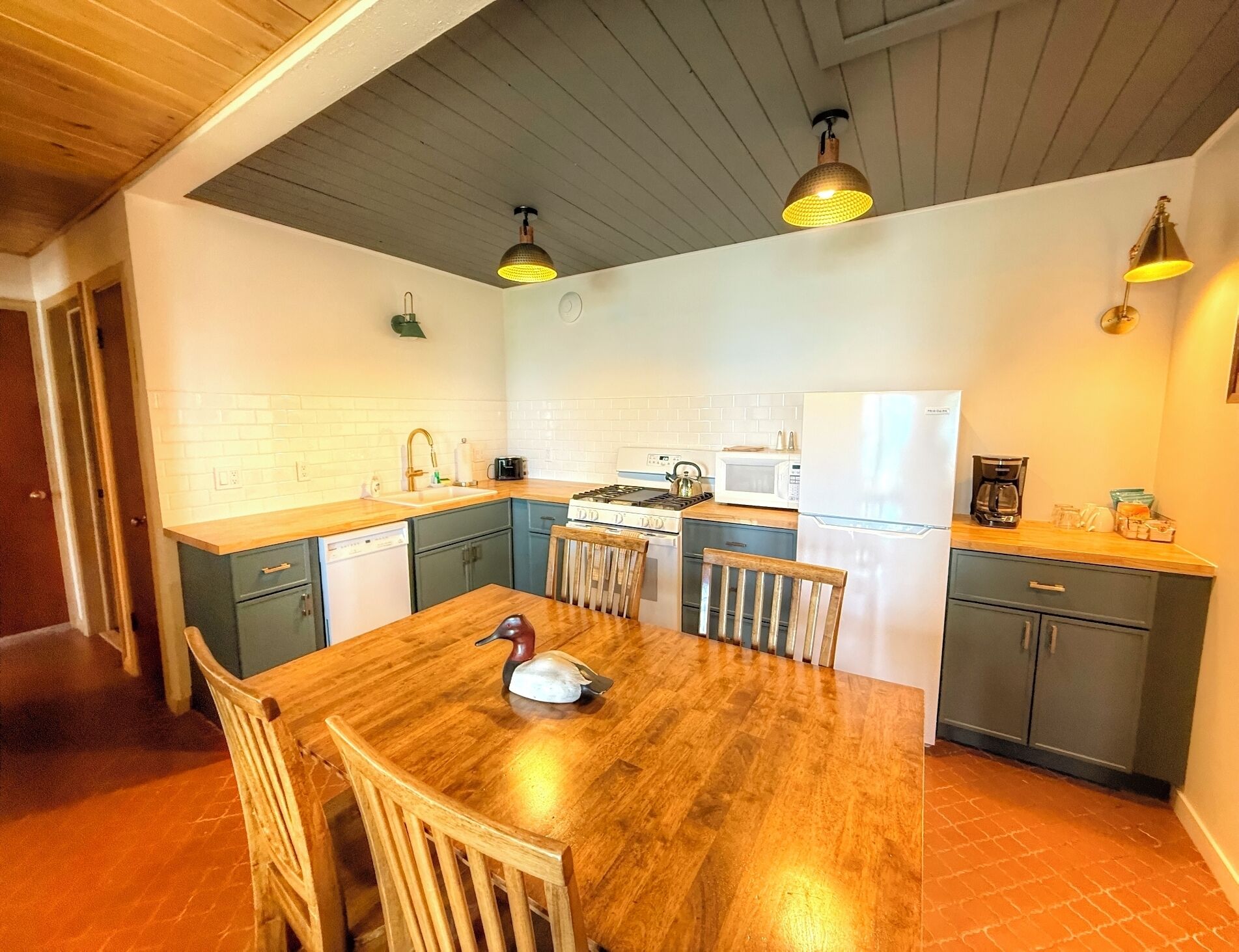 A modern kitchen with a wooden dining table, a stove, a refrigerator, and pendant lighting.
