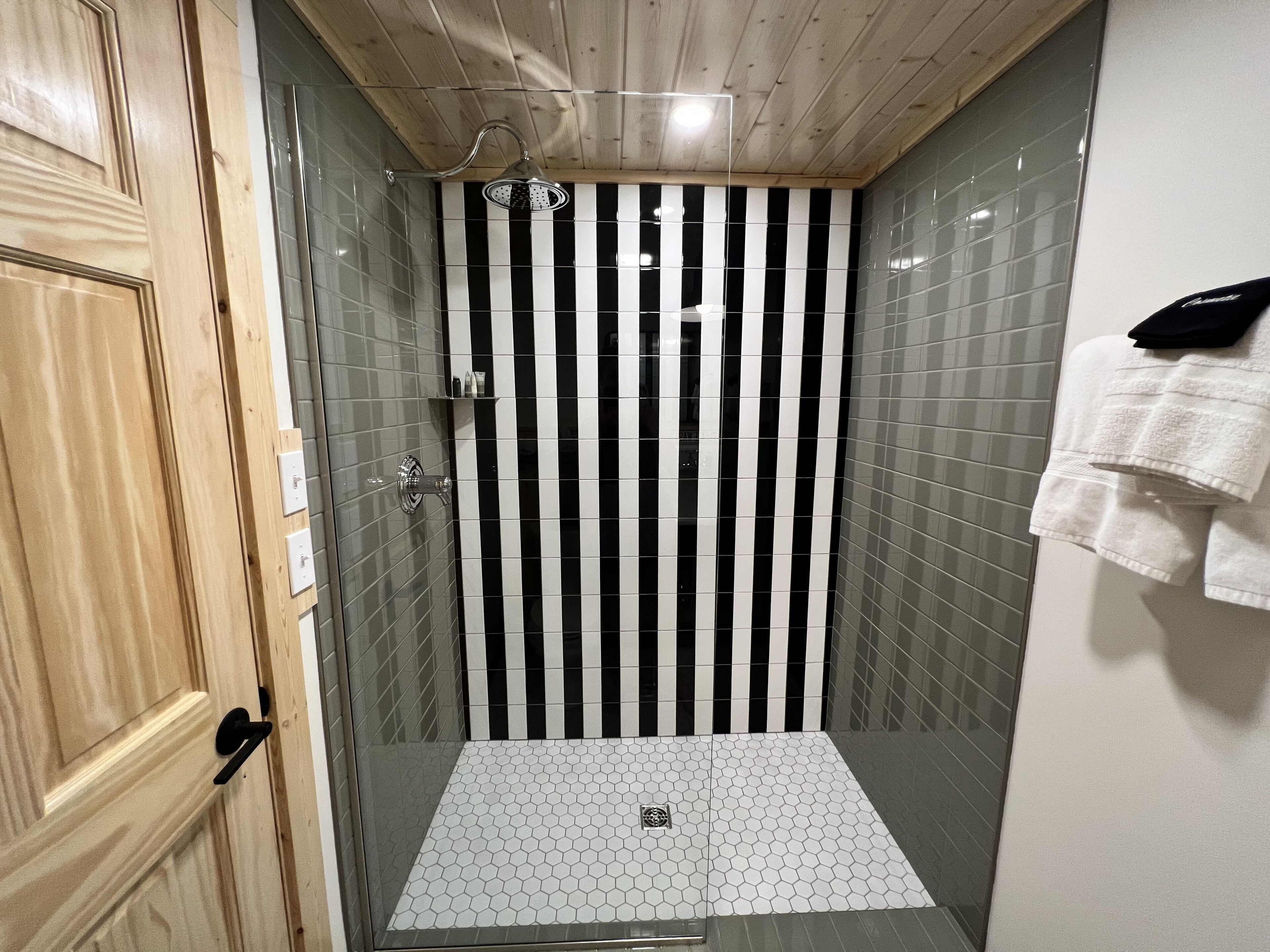 A shower with black and white striped tiles, a wooden door, and a white towel hanging on the wall.