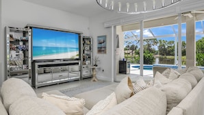Un soggiorno con una grande TV a schermo piatto, un sistema di intrattenimento integrato, un divano confortevole e vista su una piscina.