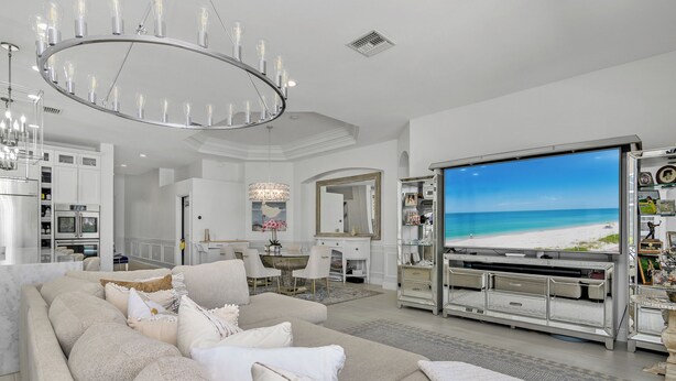 Un ampio soggiorno con una grande TV a schermo piatto che mostra una spiaggia, un moderno lampadario e un’accogliente area salotto.