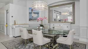 Un'area pranzo moderna con un tavolo in vetro, sedie imbottite bianche, un lampadario e un grande specchio.